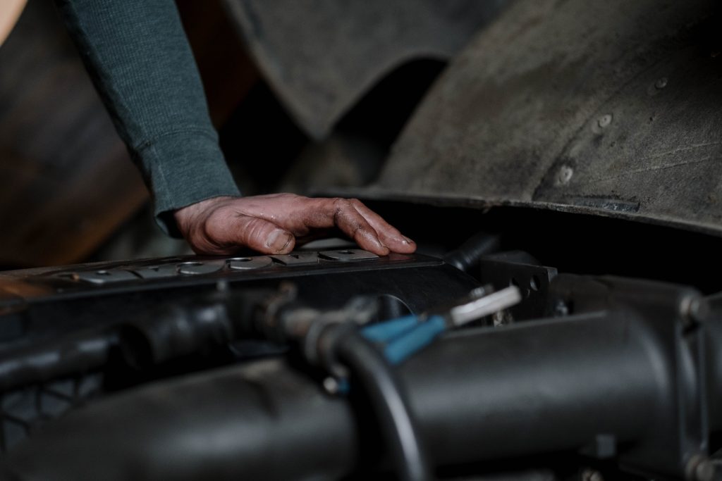 man's hand covered in grease rests on a car engine