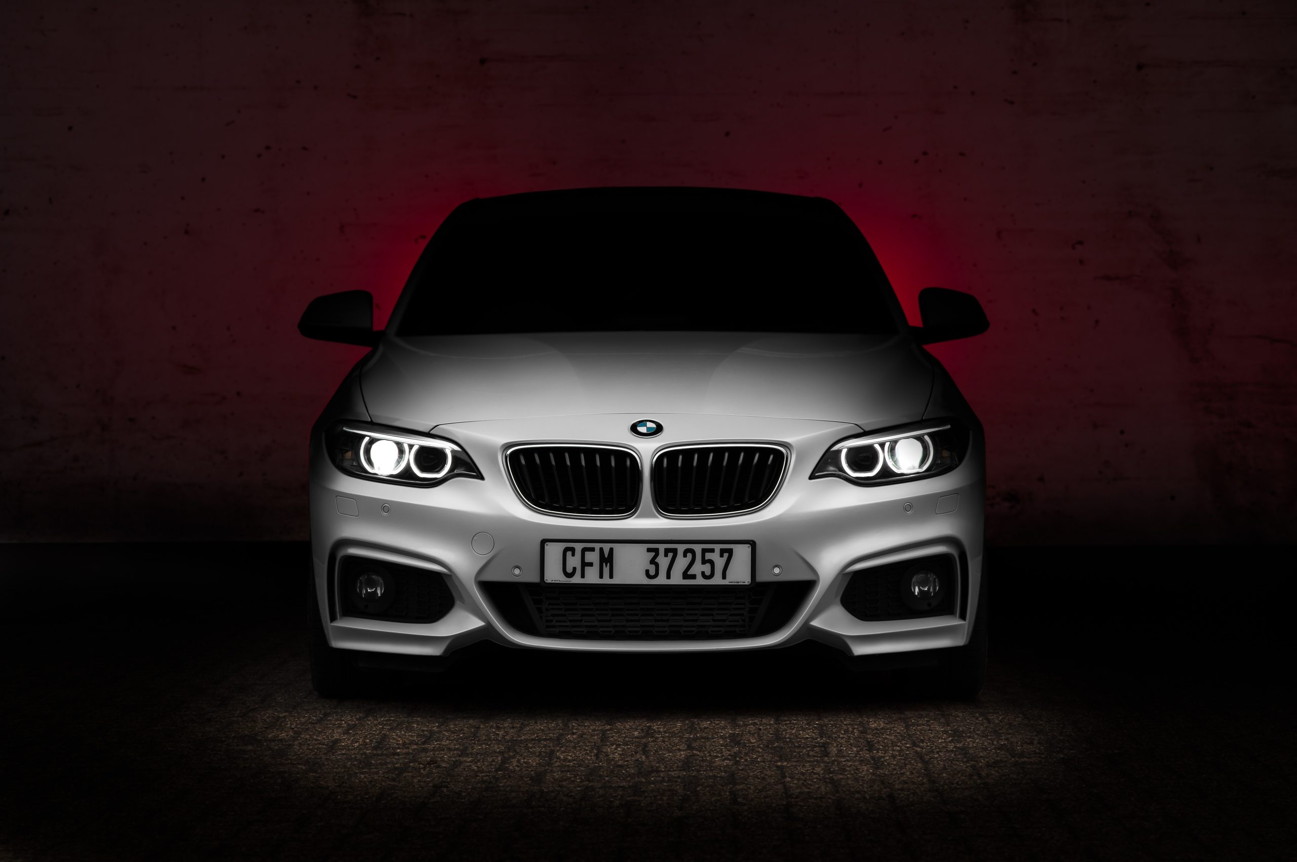 dark red background with white bmw automobile facing the camera